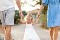 walking happy family outdoors. Parents and little blonde hair girl holding hands and walking at garden park. Rear view. Portrait. Royalty Free Stock Photo