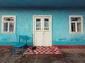 Walking stick, and a pair of old shoes and a chair on the doorstep of an aged house. Traditional rural building facade. Blue lime