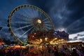 Walking Tourists close to the carousel with the Ferris Wheel in the Background on a cloudy sunset