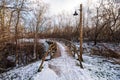 A walking trail with the first snow and footprints, wooden bridge, pole with lantern and woman with a pram in the background on Royalty Free Stock Photo