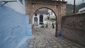 Walking under Bab El Hammar historic brick gate in blue city of Chefchaouen. Old traditional buildings around. Morocco