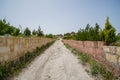 Walking unpaved rough sand road through stone brick low wall among landscape of dried and green ancient red valley with clear sky Royalty Free Stock Photo