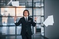 Walks in the office and throwing documents into the air. Portrait of handsome young businessman in black suit and tie Royalty Free Stock Photo