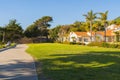 Walkway along the shore and wooden bench overlooking the ocean, and beautiful houses and green hills in the background, California