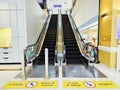 Walkway marked with yellow sidewalk with Beware of slippery floors signs at the way up and down the escalator