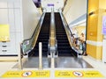 Walkway marked with yellow sidewalk with Beware of slippery floors signs at the way up and down the escalator