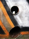 Wall with abstract graffiti in brown and white colors, with orange and black stripes and two holes filled with pipes.