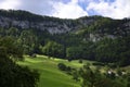 Scenic view on Jura Mountains summer landscape in Switzerland. Green meadow, old barn, coniferous trees at the foot of the rock wa