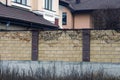 Wall of brown brick fence overgrown with dry branches of plants and grass