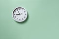 Wall clock hanging on the pale green wall with copy space. Round white clock with black hands. Five minutes to nine. Time Royalty Free Stock Photo