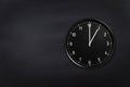 Wall clock showing one o`clock on black chalkboard background. Office clock showing 1am or 1pm on black texture