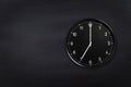 Wall clock showing seven o`clock on black chalkboard background. Office clock showing 7am or 7pm on black texture