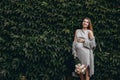 Wall of green leaves. Happy young pregnant woman holding a bouquet of flowers and her baby Royalty Free Stock Photo