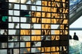 Wall made of polished metal mirrored rectangles imitating brickwork. Interior element and silhouette of people in the background. Royalty Free Stock Photo