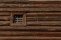 The wall of an old log house with a small window behind bars Royalty Free Stock Photo