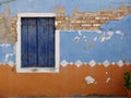 A wall with paint peeling and window with blue shutters Royalty Free Stock Photo