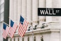 Wall Street sign post with American national flags in background. New York city financial economy district, stock market trade