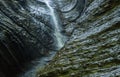 Wall of a waterfall in sunlight cave background. Falling water on the background of weathered wet wall, stone texture