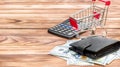 Wallet with money, shopping cart and calculator on the wooden background. Space for text