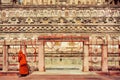 Walls of carved historical Budhist temple and lonely walking monk in yellow red dress near the gate, India.