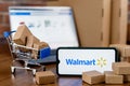 Walmart is an American multinational retail corporation. Smartphone with Walmart logo on the screen, shopping cart and laptop