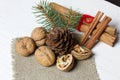 Walnuts, cinnamon sticks and spruce branch with pine cone. Lying on a piece of linen. Against the background of white painted