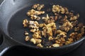 Walnuts cooking in a cast iron frying pan on a ceramic hob