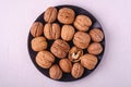 Walnuts heap food in black plate with half peeled nut on white background