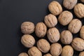 Walnuts in the shell on black surface, top view. Background of round walnuts. Healthy nuts and seeds composition. Royalty Free Stock Photo