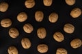 Walnuts in the shell on black surface, top view. Background of round walnuts. Healthy nuts and seeds background. Royalty Free Stock Photo