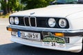 A vintage BMW E30 325i convertible stands in the parking lot. Front view of the grille, hood, headlights and bumper.