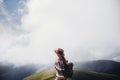 wanderlust and travel concept. girl traveler in hat with backpack looking at clouds in mountains. stylish hipster woman exploring Royalty Free Stock Photo