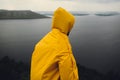 Wanderlust and travel concept. Hipster traveler in yellow raincoat standing on cliff and looking at lake in windy moody day. Man Royalty Free Stock Photo