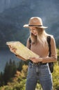 Wanderlust and travel concept. Stylish traveler girl in hat looking at map, exploring woods