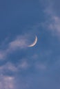 Waning crescent moon reflecting golden light from the sunset as wispy clouds pass in front.