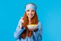 Wanna bite. Cute feminine young redhead girl in glamour nightwear, sleep mask, prepare breakfast, holding spoon and bowl