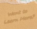 Want to Learn More? Sign on the sand on the beach with the sea washing up the shore Royalty Free Stock Photo