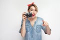 Want to make photoshout. Young blogger girl in casual denim shirt with makeup, red headband standing, holding retro camera and