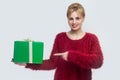 Want you? Portrait of happy young woman in red blouse standing and holding green gift box and pointing finger, looking at camera Royalty Free Stock Photo