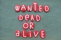 Wanted, dead or alive, creative slogan composed with red colored stone letters over green sand