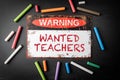 WANTED TEACHERS. Metal warning sign and colored pieces of chalk on a dark chalkboard background Royalty Free Stock Photo