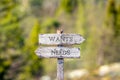 wants needs text carved on wooden signpost outdoors in nature.