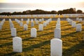 War cemetery with rows of white marble graves on green grass at sunset with ocean view. Marine veteran's cemetery