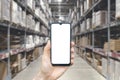 Warehouse with a hand holding an empty smartphone. Blurred industrial warehouse with goods and products. Logistics Royalty Free Stock Photo