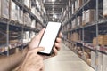 Warehouse with a hand holding an empty smartphone. Blurred industrial warehouse with goods and products. Logistics Royalty Free Stock Photo