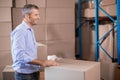 Middle-aged man in blue shirt and jeans stacking sealed boxes on blue metal shelving in warehouse Royalty Free Stock Photo