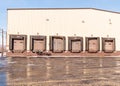 A warehouse with six loading docks with closed doors reflecting off of a wet parking lot on a sunny winter day Royalty Free Stock Photo