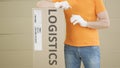 Warehouse worker with big parcel with printed LOGISTICS text and label on it