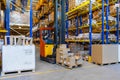 Warehouse worker driving a forklift truck full of goods between high blue yellow steel shelves inside warehouse