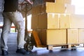 Warehouse worker with hand pallet truck unloading shipment boxes on pallet.